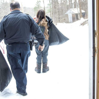 Member of law enforcement carries a bag next to a woman carrying a bag as they exit her home